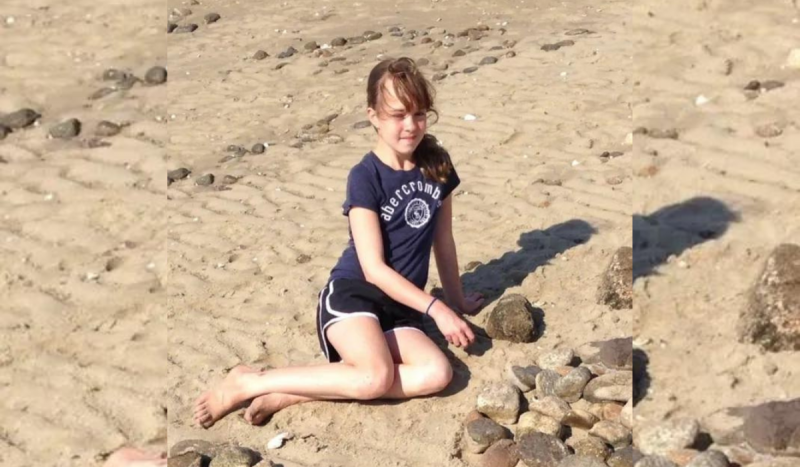 Foto mostra menina com roupa azul deitada na areia da praia