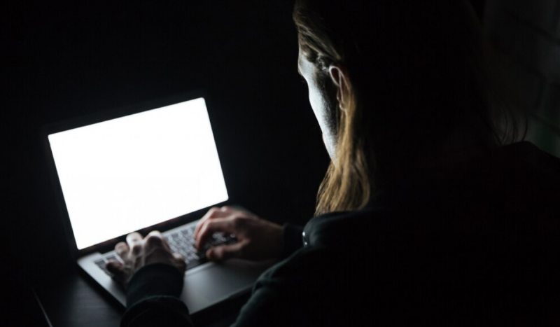 Foto mostra mulher de costas no escuro mexendo no notebook em cima da mesa para ilustrar matéria sobre cadastro de pedófilos em SC