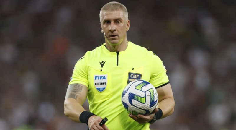 Árbitro brasileiro Anderson Daronco aparece com bola na mão durante partida de futebol