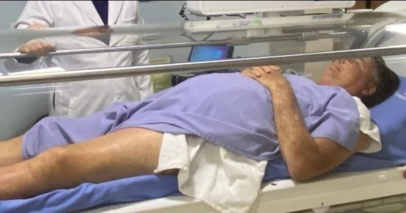 Homem deitado em leito de hospital usando roupão azul - Foto mostra ex-presidente Jair Bolsonaro 