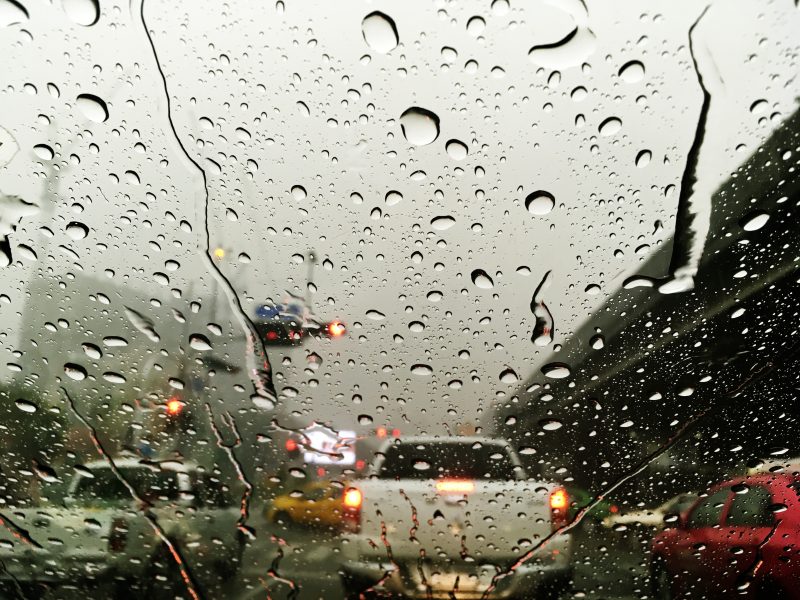 Foto mostra gotículas de água da chuva em vidro de carro que está no trânsito
