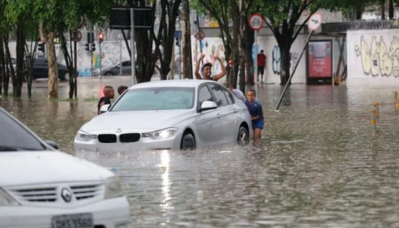 na imagem aparecem pessoas e carro tentando dar marcha ré para sair da enchente