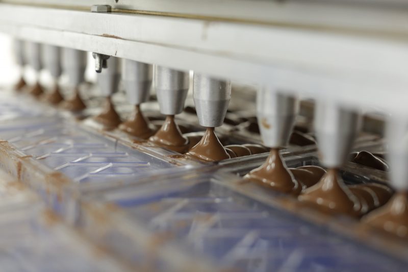 Foto de ponteiras de uma máquina colocando chocolate dentro de forma de plástico para fazer barras de chocolate 