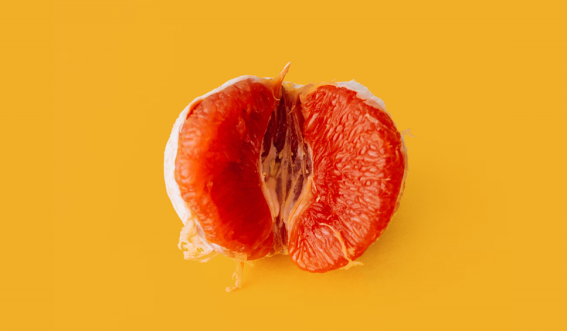 Foto mostra laranja vermelha aberta como se fosse uma vagina, em frente a fundo amarelo vibrante. Imagem é usada para ilustrar procedimentos íntimos feitos em Florianópolis
