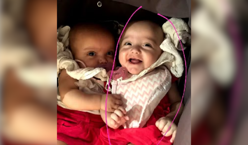 Foto mostra duas bebês agarradas. Uma gêmea sorri para a foto