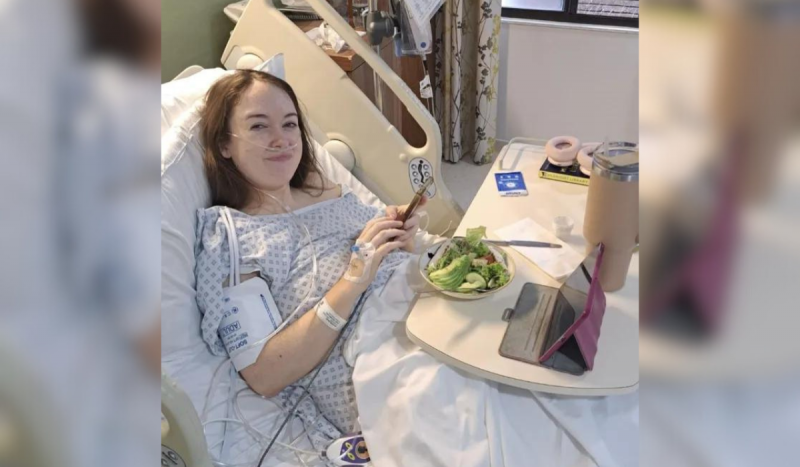 Paciente com roupa hospitalar internada e deitada em cama, enquanto come salada