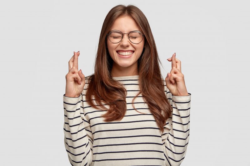 mulher com os dedos cruzados e com os olhos fechados e sorrindo representando maré de sorte 