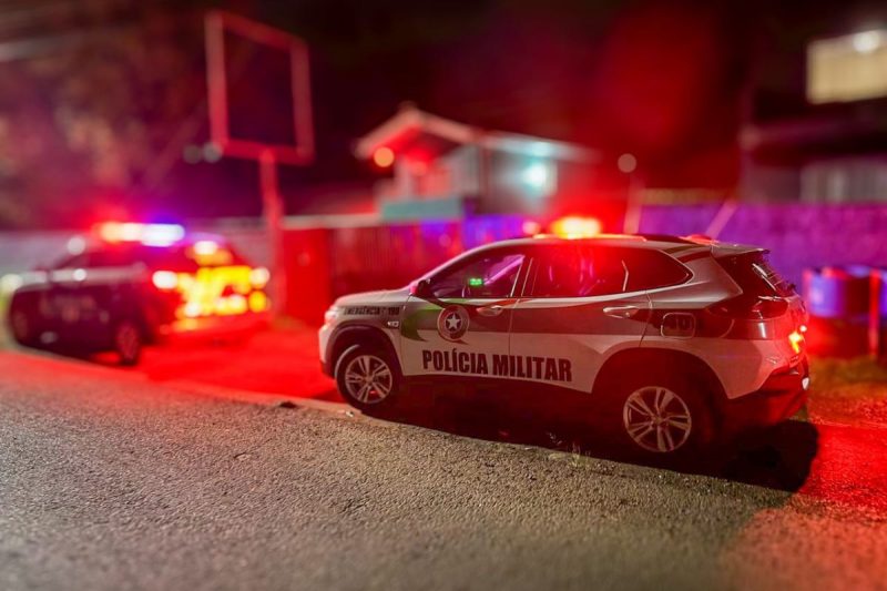 dois carros de polícia com sirenes ligadas a noite, estacionados em uma rua em frente ao bar suspeito de exploração sexual