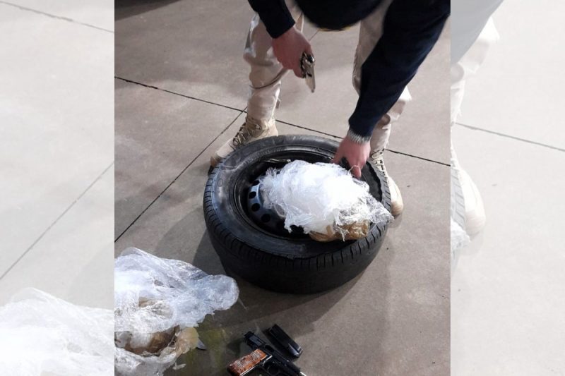 pistolas escondidas em pneu estepe de carro; na imagem aparecem as mãos de um policial rodoviário federal; em uma delas ele segura o pneu, na outra uma pistola; no pneu estão sacos plásticos onde estavam enroladas as duas pistolas; no chão aparece outro saco plástico 