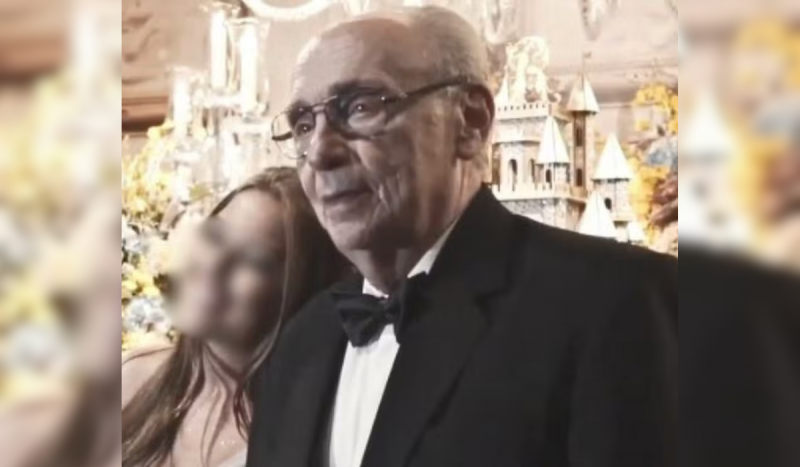 Homem idoso de cabelos grisalhos usando terno preto e gravata borboleta enquanto posa para foto em frente a flores e decorações brilhantes. Foto de Renato Roberto Cuoco é usada para ilustrar matéria sobre os herdeiros do Itaú