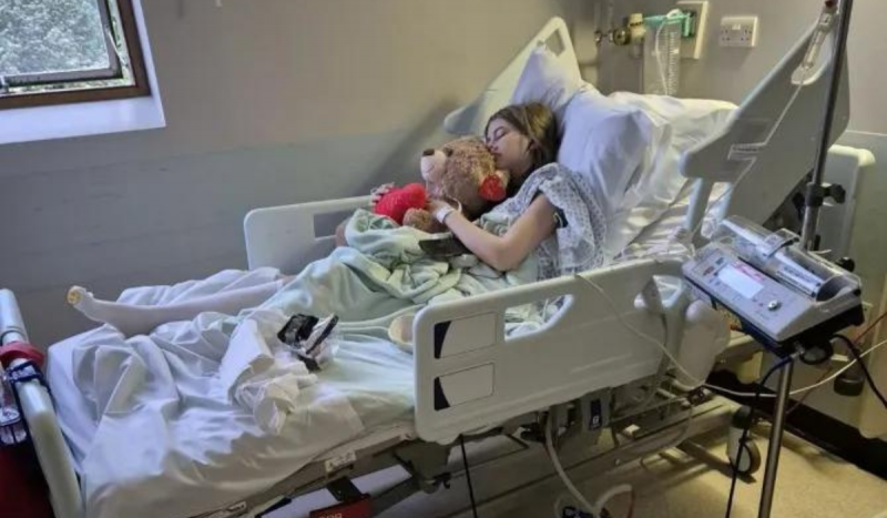 Foto mostra paciente deitada em leito de hospital abraçada em urso de pelúcia