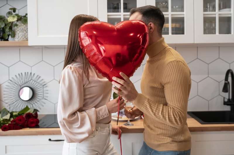 Homem e mulher se beijando atrás de um balão vermelho em forma de coração