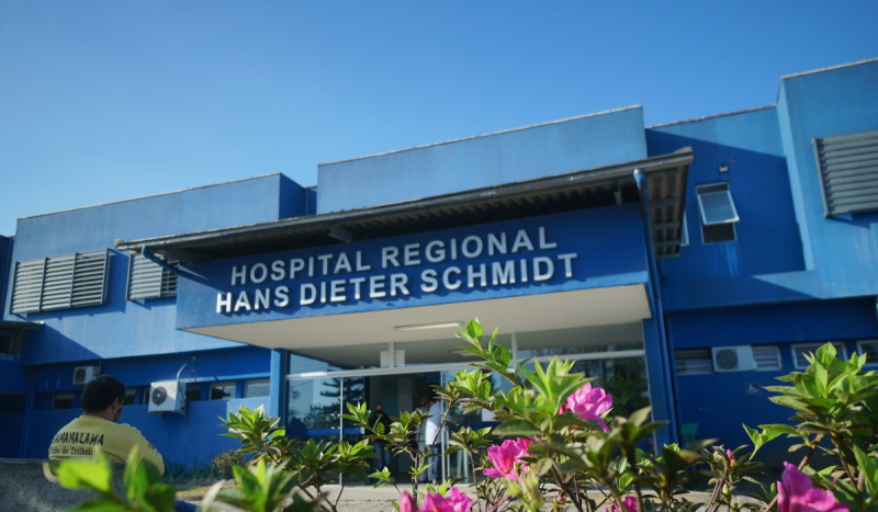 Fachada do Hospital Hans Dieter Schmidt, em Joinville, SC - Prédio com fachada azul e flores na cor lilás na parte inferior a foto. Imagem é utilizada para ilustrar matéria sobre edital da Secretaria da Saúde de SC