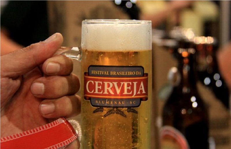 Homem segurando copo com emblema do festival brasileiro da cerveja de Blumenau