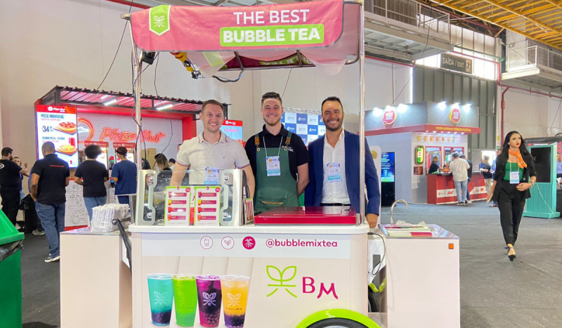 Representantes da marca Bubble Mix - três homens brancos sorriem de pé atrás de um carrinho de chá que funciona como expositor na ABF Franchising Expo 2024