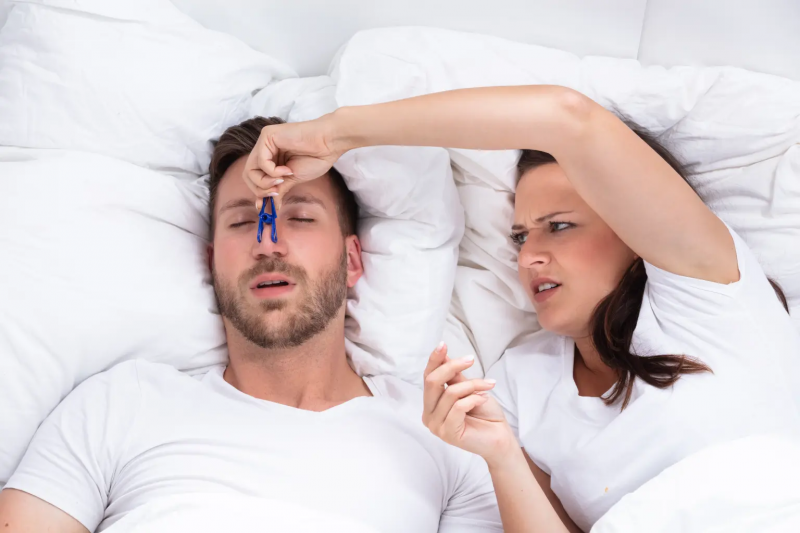 A woman places a clip on a man's nose to see if he will stop snoring