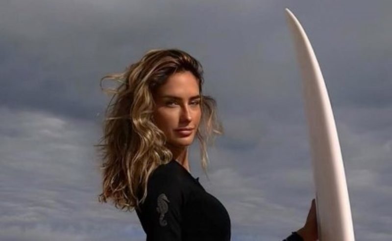 na foto Isabella settanni aparece segurando uma prancha de surfe, esporte que aprecia 