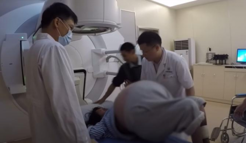 Médicos usando jalecos e máscaras descartáveis colocam paciente com barriga muito inchada dentro de equipamento para fazer exame de imagem