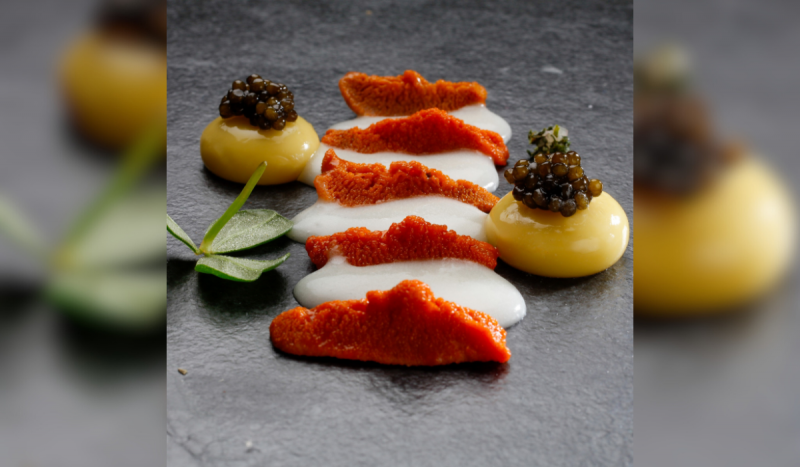 Foto mostra creme branco em cima de superfície preta, duas gemas uma de cada lado do creme e ovas de peixe em cima delas