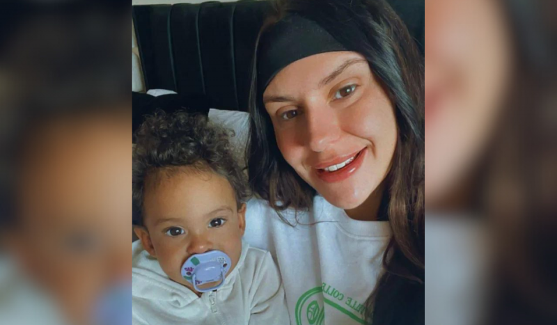 Foto mostra mulher branca sorrindo segurando bebê no colo. Ela sorri usando uma camisa branca e a bebê usa um moletom branco. Foto é utilizada para ilustrar matéria sobre o diagnóstico de câncer incurável da mulher