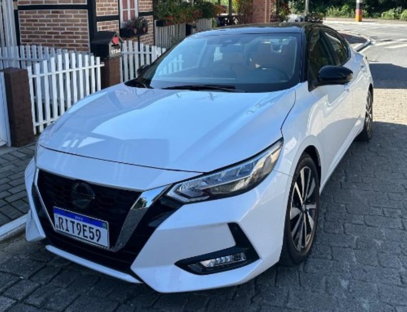 na foto, Carro Nissan Sentra 2024 aparece com ângulo de lado estacionado na rua perto de uma casa