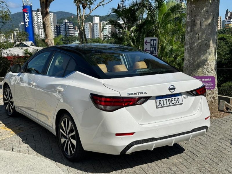 Nissan Sentra aparece estacionado perto de árvore em foto e mostra o carro do ângulo de trás com o porta-malas 
