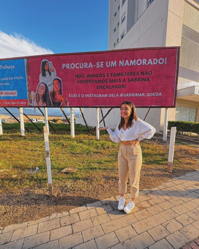 Influencer posa ao lado do outdoor