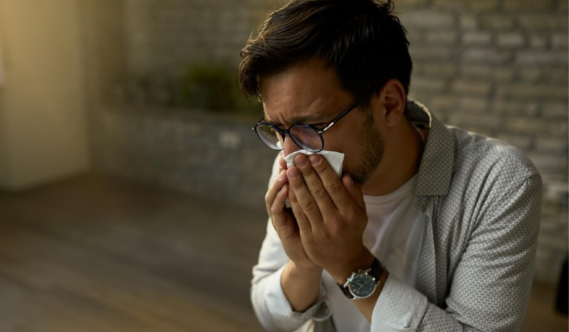 A imagem mostra um homem espirrando por causa da alergia a gato