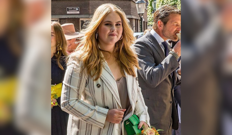 Mulher branca e loira usando blazer branco com listras enquanto caminha pela rua em meio à multidão