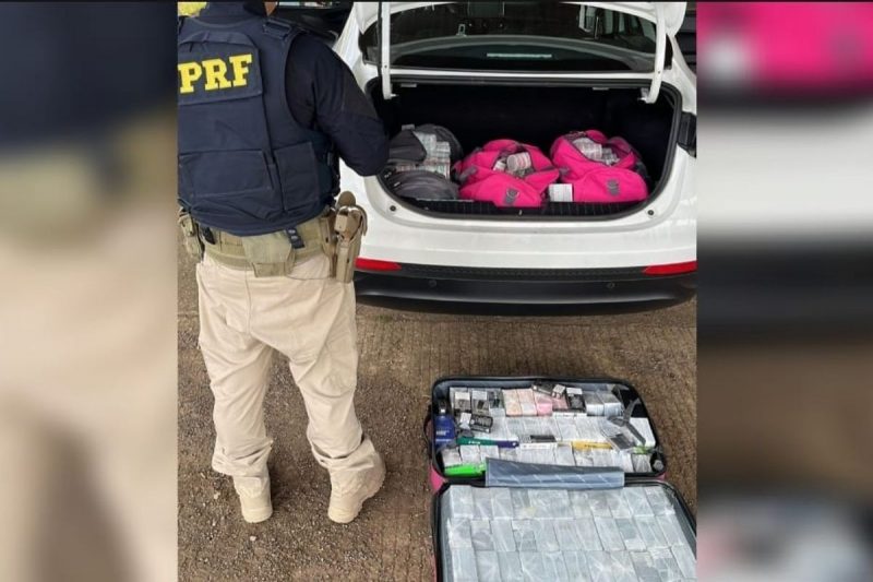 Produtos contrabandeados em porta-malas do carro, policial rodoviário federal em pé de costas, mala no chão com produtos 