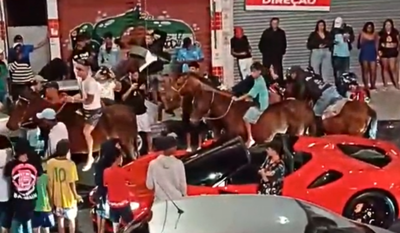 Foto mostra multidão em rua e cavalos montados por jovens de bermuda. Na foto também é possível ver um carro de luxo vermelho durante baile funk do PCC