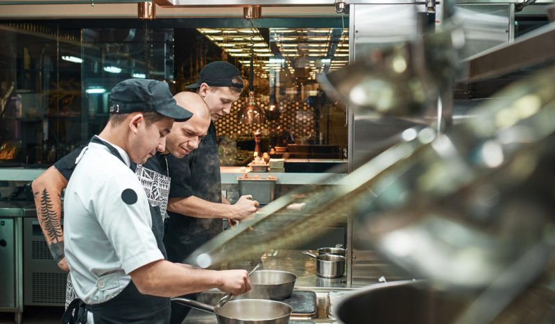 Cozinheiros uniformizados manipulando alimentos na cozinha do restaurante