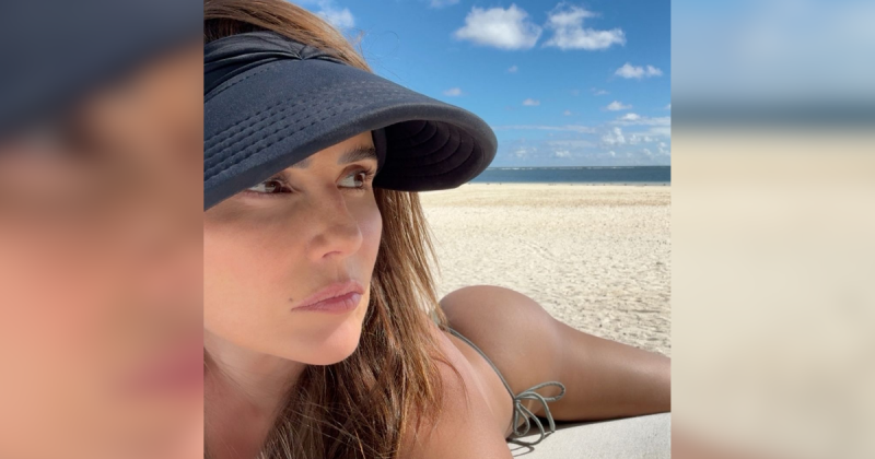 Atriz Deborah Secco posando deitada por cima da areia em praia