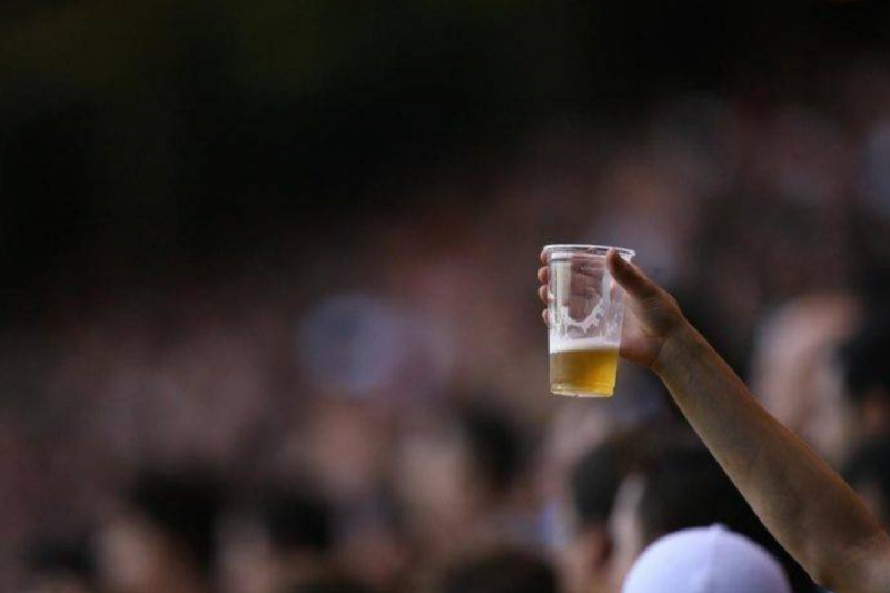 Copo de cerveja em primeiro plano, em um estádio de futebol