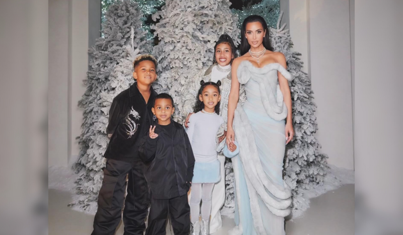 Kim Kardashian e os filhos, um deles foi diagnosticado com vitiligo - foto mostra uma mulher negra de cabelos pretos em pé usando vestido prateado, ao lado de crianças, dois meninos com casacos e calças pretas e uma menina com roupa prateada também, todos em pé