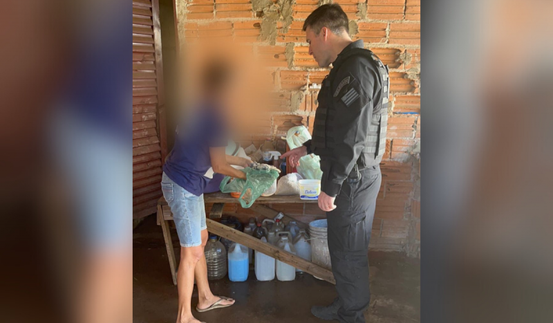 Mulher com cabeça borrada mostrando produtos de limpeza para policial fardado com roupa preta