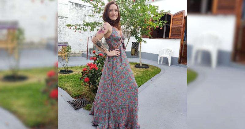 Carolina Arruda, uma jovem que sente as piores dores do mundo, vestida com um vestido florido, com um jardim atrás dela