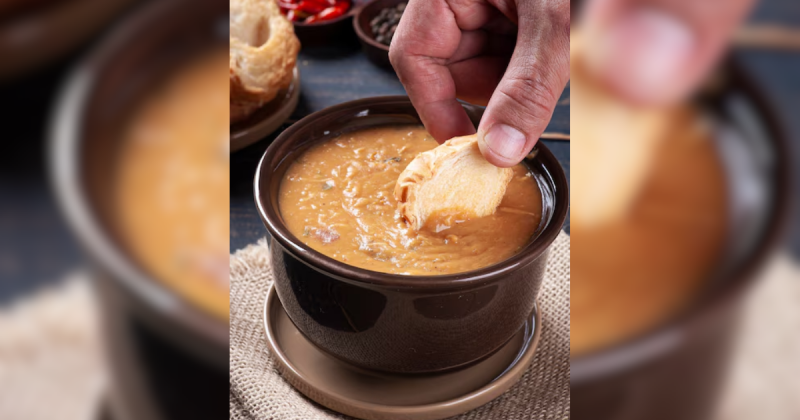 Tigela com sopa e uma mão com pão sendo molhado na sopa