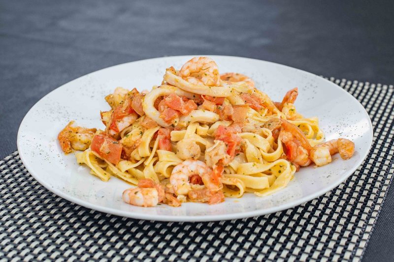 Foto de um prato com macarrão, camarões e lulas, servido em um prato branco sobre uma mesa cinza. O prato é do restaurante Villa Italia, em Balneário Camboriú. 