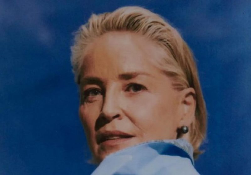 na foto aparece a atriz sharon stone com um brinco e olhando para frente com casaco azul