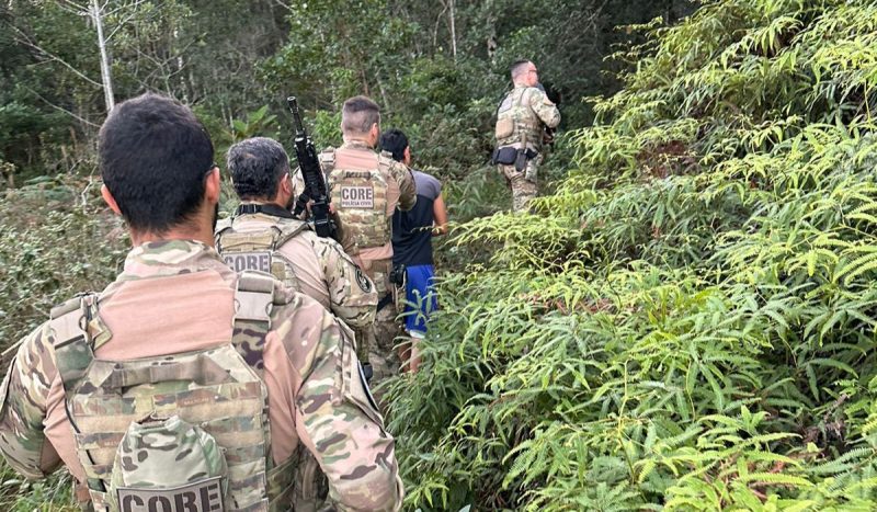 foto mostra policias conduzindo venezuelano em área de mata