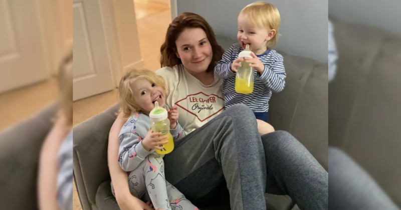 Mulher com os dois filhos no colo tomando suco amarelo