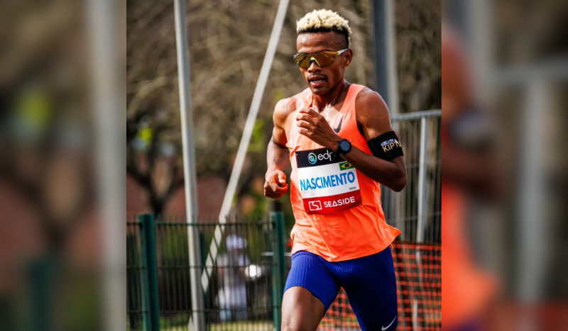 Homem negro com cabelo loiro correndo vestindo uma regata laranja neon e shorts colantes azuis