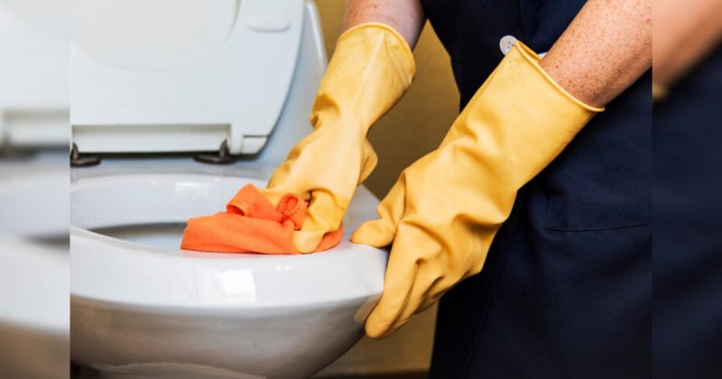 Pessoa de luvas limpando vaso sanitário com flanela laranja