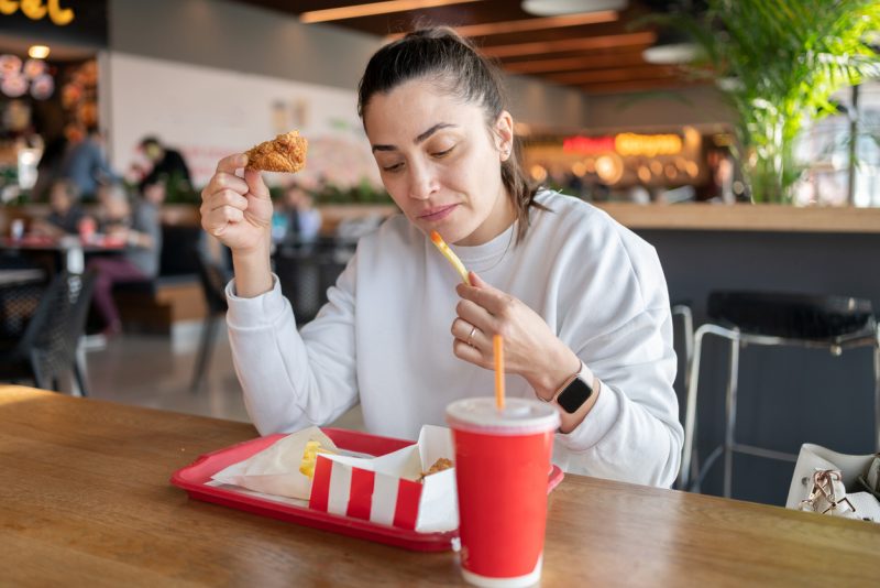 Mulher comendo frango frito e batata frita em praça de alimentação