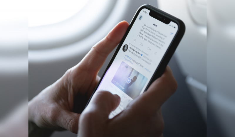 Pessoa mexendo no X, antigo Twitter, pelo celular num avião