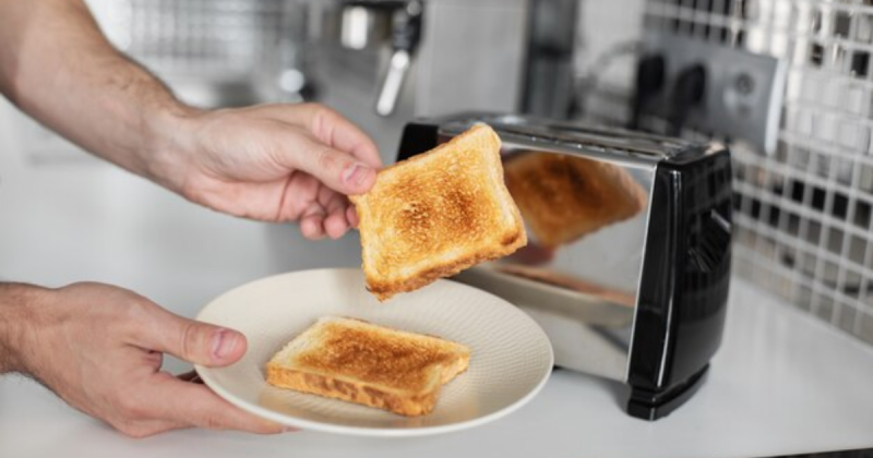 Torradeira com dois pães perto e mãos 