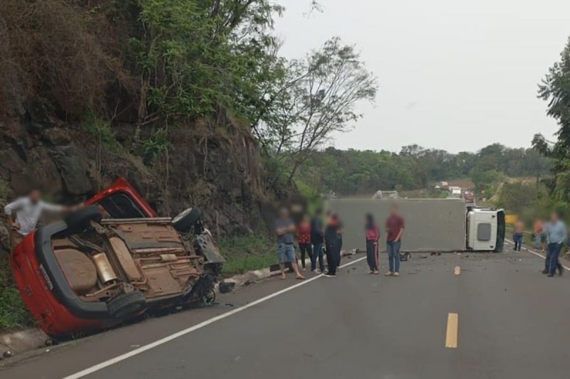 carro capotado às margens da rodovia SC-157 e caminhão tombado e trancando a rodovia, pessoas no meio da rua olhando a cena do acidente