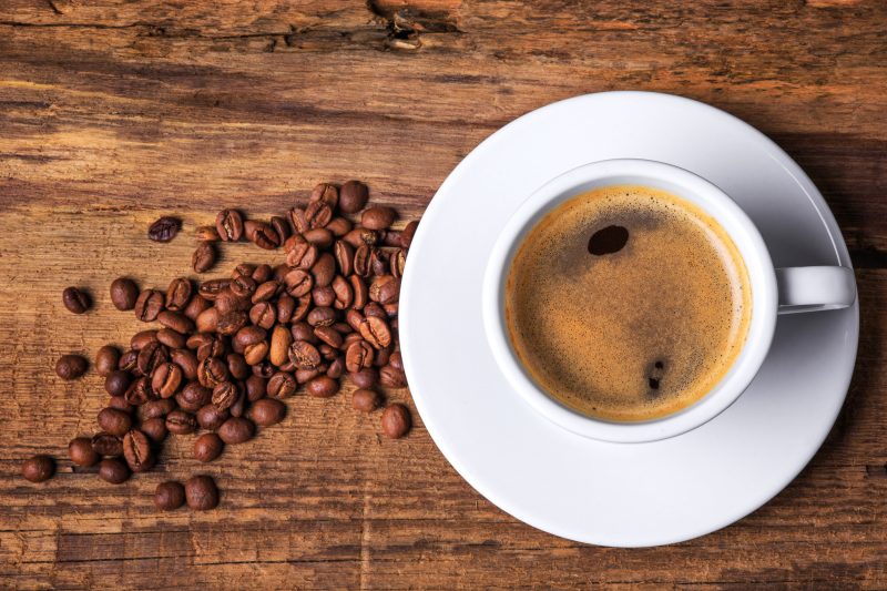 Xícara de café sobre uma mesa de madeira ao lado de seus grãos