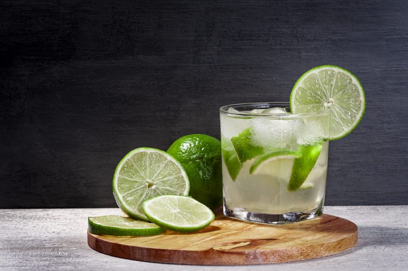 Dia da Cachaça: Caipirinha brasileira em uma tábua de corte com limão com fundo gradiente, espaço de cópia